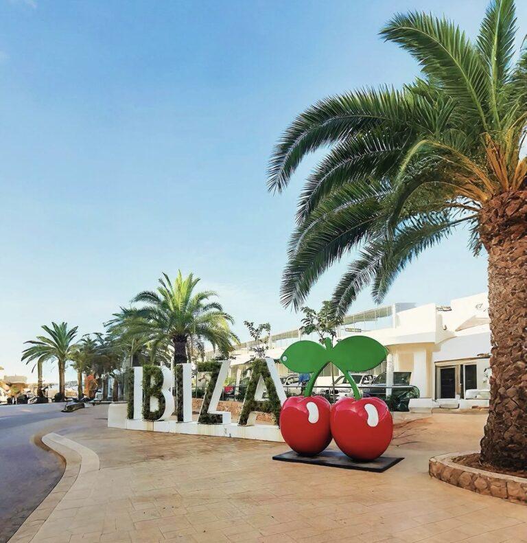 Ibiza sign and palm trees outside a white hotel.